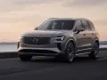 Elegancki, szary Volvo CX90 jedzie po drodze nad jeziorem o zachodzie słońca.