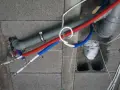 Instalacja wodna z rurami PP w ścianie z pustaków. Widoczne rury czerwone i niebieskie, szary odpływ.