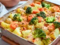 Pieczone ziemniaki, marchewka i brokuły w naczyniu żaroodpornym, posypane przyprawami.