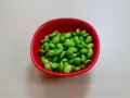 Czerwona miseczka pełna zielonych ziaren soi. Czy to edamame? Tak, to właśnie edamame, zdrowe i pyszne!