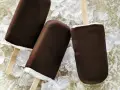 Drei Schokoladen-Vanilleeis am Stiel liegen auf Eiswürfeln.