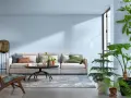 Jasny salon z wygodną kanapą, stolikiem kawowym i dużą ilością roślin. Sufit w kolorze ścian tworzy spójną, spokojną atmosferę.