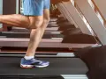 Gambe muscolose in movimento su un tapis roulant, simbolo di corsa indoor e allenamento.