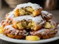 Buñuelos de manzana dorados y esponjosos, espolvoreados con azúcar glas. Un bocado dulce y crujiente.