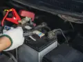 Ręka w białej rękawicy podłącza kabel do akumulatora, pokazując, jak odłączyć akumulator.