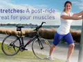 A woman performs a bicycle stretch, leaning on a pole after a ride by the beach.