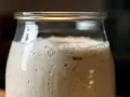 Ein Glas mit schaumigem Sauerteig, der sich nicht verdoppelt. Kleine Bläschen und eine cremige Textur sind sichtbar.