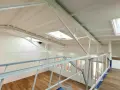 Widok z antresoli na jasne wnętrze z drewnianą podłogą, oknami i świetlikami w dachu.