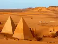 Pustynny krajobraz Sudanu z piramidami i dwoma podróżnikami na wielbłądach.