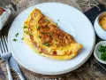 Goldbraunes Omelett mit Käse und Schnittlauch, perfekt für ein schnelles Omelette Rezept. Daneben Eier, Käse und Schnittlauch.