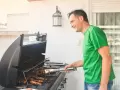 Glad man grillar korv på balkong.