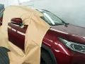 Voiture rouge bordeaux masquée pour la peinture. On se demande combien de temps entre peinture et vernis pour un tel travail.