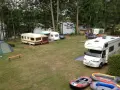 Campingplatz am sonnensee flachslanden mit Wohnmobilen, Wohnwagen, Zelt und Schlauchbooten am Ufer.