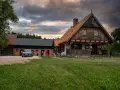 Szelągówka camping: drewniane domki i budynki gospodarcze, samochód na żwirowym podjeździe, zachmurzone niebo.