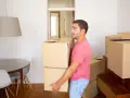 Un homme porte des cartons, prêt à quitter le domicile conjugal. Le propriétaire semble pensif, entouré de cartons de déménagement.