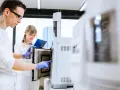 W laboratorium młoda para naukowców pracuje przy aparaturze. On w okularach, ona z notatkami.