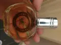 Szklana butelka z bursztynowym płynem, ozdobiona okrągłą etykietą z wizerunkiem statku i napisem "Christopher Columbus perfumy".