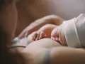 Ein Baby stillt, die kleinen Finger greifen sanft zu. Ein Moment der Ruhe und Verbundenheit.