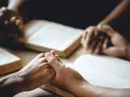 Hände halten sich über aufgeschlagenen Bibeln, ein Zeichen dafür, wie beten Christen: in Gemeinschaft, mit Glauben und Hoffnung.