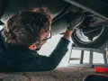 Un giovane impara come si diventa meccanico, lavorando sotto un'auto con attrezzi e spray.