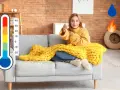 Donna sul divano con coperta gialla, termometro e icone di acqua e fuoco. Soluzione per deumidificare e riscaldare contemporaneamente.