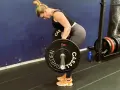Kvinna utför en t bar row med en skivstång i ett gym.