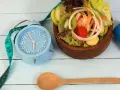 Réveil bleu, ruban à mesurer, salade fraîche et haltère bleu. L'heure est à la forme, jeune 16/8.
