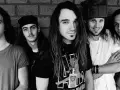 Cinq membres du groupe Pearl Jam posent devant un mur de briques. L'un d'eux porte un t-shirt avec le logo du groupe.