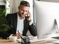 Uomo d'affari al telefono, scrive appunti. Potrebbe essere un agente immobiliare che discute di quanto guadagna un agente immobiliare.