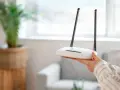 Dłoń trzyma biały router z dwiema antenkami. Dowiedz się, jak zresetować router, aby rozwiązać problemy z siecią.