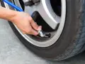 Mano che collega un tubo blu alla valvola di un pneumatico per controllare la pressione gomme auto.