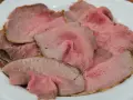 Fette sottili di arrosto di manzo rosa e succulento, servite su un piatto bianco.