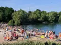Ein sonniger Tag am **Badesee Bonn**. Viele Menschen genießen das Wasser und den Strand, umgeben von grünen Bäumen.
