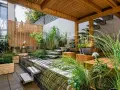Giardini fioriti idee: un angolo zen con vasca d'acqua, gradini in pietra, sedute in legno e piante rigogliose sotto un pergolato.