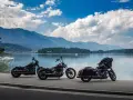 Tre moto parcheggiate sul lungolago, pronte per il faaker see motoraduno. Montagne sullo sfondo, cielo azzurro con nuvole bianche.