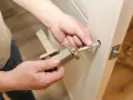 Hands assembling a modern door handle. A metal spindle is being inserted into the door mechanism, showing how to replace door handle.