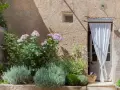 Lavendel beet ideen: Ein mediterraner Garten mit Rosen, Lavendel und einer Tür mit weißem Vorhang.
