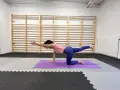 Kobieta na macie ćwiczy pozycję "ptak-pies", unosząc rękę i nogę. To świetny sposób na ćwiczenie równowagi i stabilizacji, idealne do stretchcare jak podawać.
