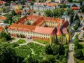 Widok z lotu ptaka na klasztor w Trzebnicy z charakterystycznymi żółtymi murami i czerwonymi dachami. Otoczony zielenią i budynkami miejskimi.