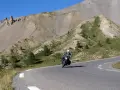 Motociclista percorre la route de grand alpes tra montagne scoscese e cielo azzurro.