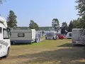Solig dag på camping norrlandskusten med husbilar och husvagnar uppställda nära vattnet.