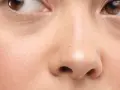 Nahaufnahme eines Gesichts mit braunen Augen und einer normalen Hautstruktur, die leichte Falten um die Augen zeigt.