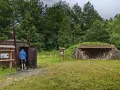 Odwiedziny w muzeum wypału węgla drzewnego. Człowiek wchodzi do zabytkowego pieca, obok zadaszenie z drewnem.