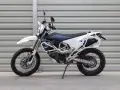 Biało-niebieski motocykl Husqvarna z bagażnikiem, gotowy na przygody w terenie. To idealny sprzęt do lekkiego enduro.