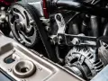 Close-up of a car engine showing a toothed drive belt wrapped around a pulley and connected to an alternator.