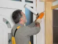 Montaż drzwi wewnętrznych z ościeżnicą regulowaną. Fachowiec uszczelnia pianką montażową przestrzeń między ścianą a drewnianą ościeżnicą.
