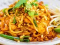 Un delicioso plato de pad thai con fideos de arroz, pollo, brotes de soja, cacahuetes picados y cilantro fresco.