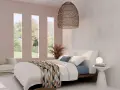 Habitación con cama blanca y manta geométrica. Tres ventanas verticales dejan ver un jardín. El espacio, con tonos neutros, evoca la serenidad de los cuartos blancos.