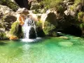 Cascada de agua cristalina cayendo en unas pozas turquesas, rodeadas de rocas y vegetación exuberante.