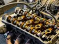 Close-up of an engine's camshafts, showing the intricate metalwork involved in camshaft repair. The golden-brown oil coating suggests recent maintenance.